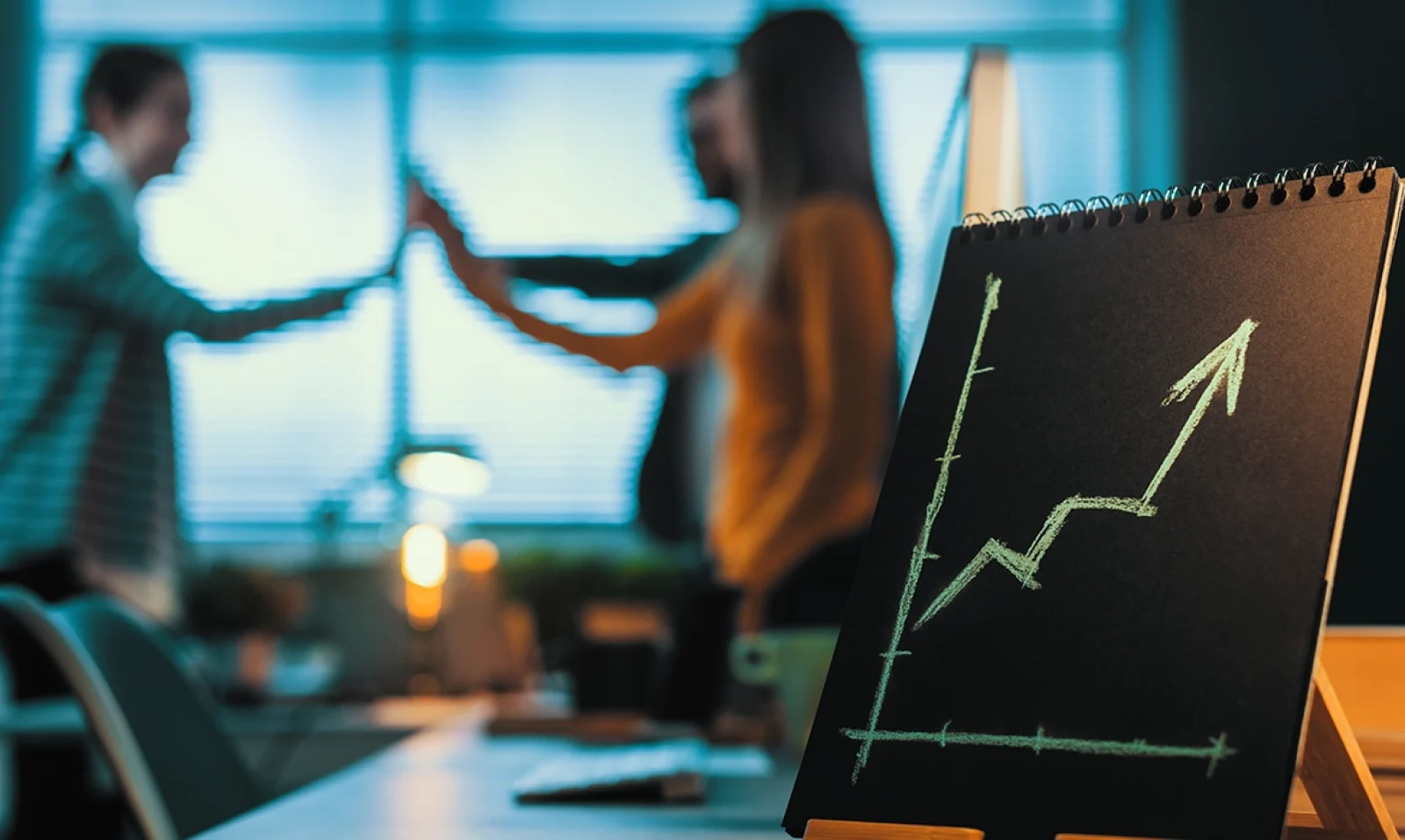 Gráfico de crecimiento empresarial con flecha ascendente en una oficina con un equipo de trabajo celebrando al fondo.