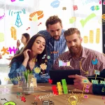 Equipo de negocios reunido en torno a una tablet, con bocetos gráficos de colores sobre crecimiento y datos alrededor.